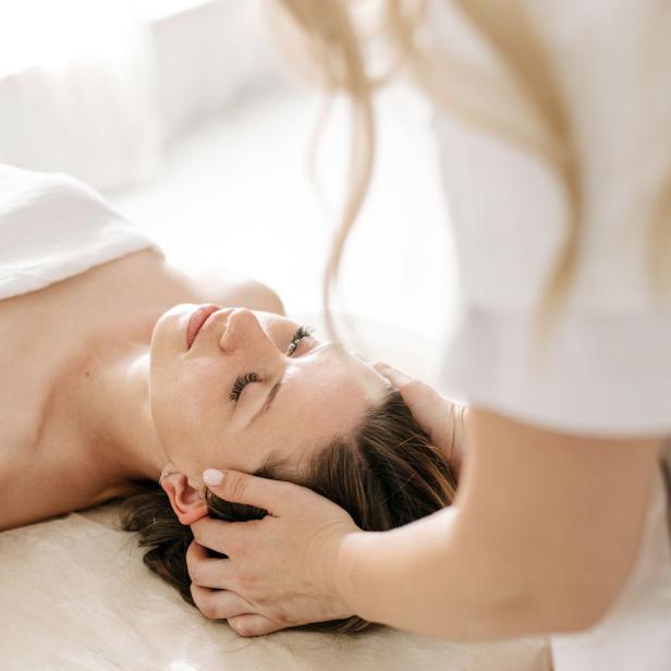 Eine Kundin liegt entspannt bei einer Kopfhautmassage im Spa, während eine Behandlerin ihren Kopf hält.
