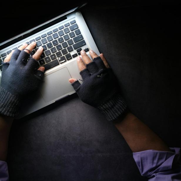 Hände in Fingerloshandschuhen tippen auf einem Laptop.