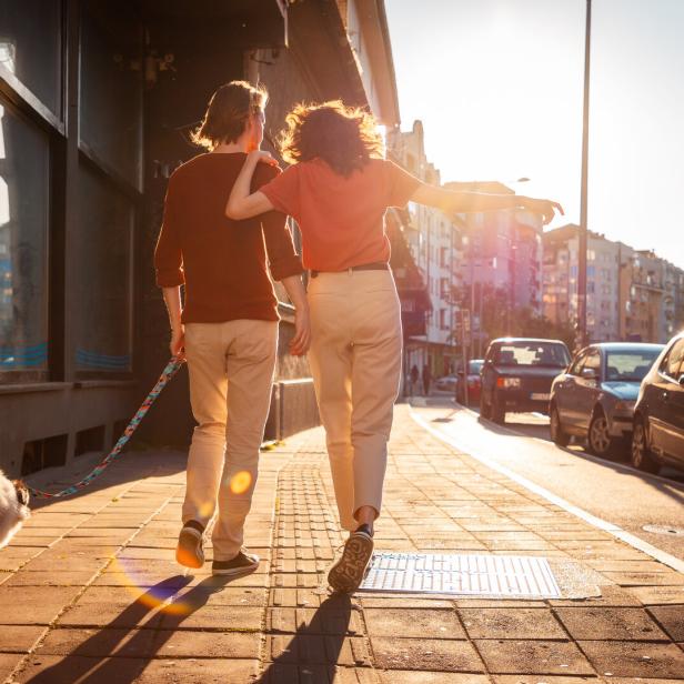 Back view of couple man and woman is walking around city with their dog. Sunset light in background