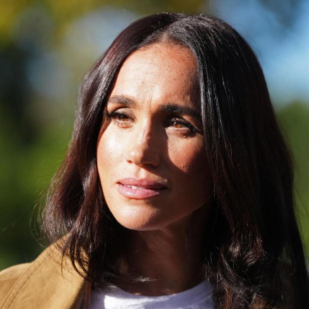 Meghan Markle blickt mit ernstem Ausdruck vor einem unscharfen, grünen Hintergrund in die Ferne.