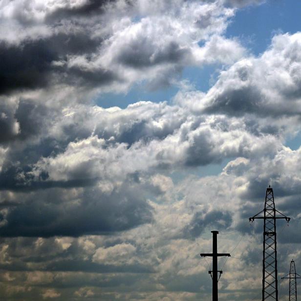 Strommasten ragen vor einem dramatischen, wolkenverhangenen Himmel in die Höhe.