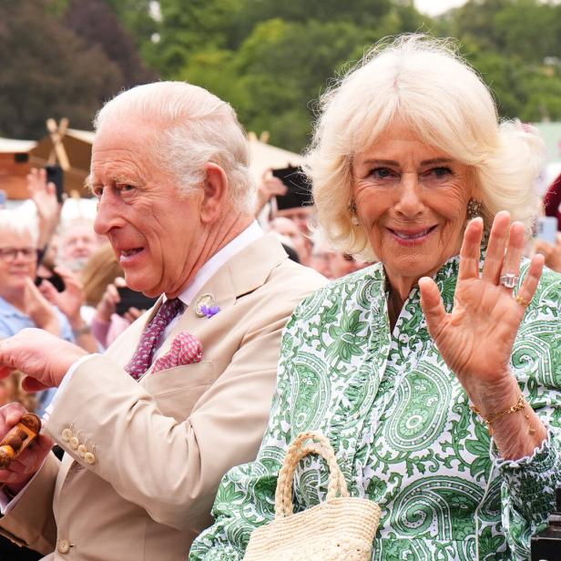 König Charles III. und Königin Camilla winken in einer Kutsche einer Menschenmenge zu.
