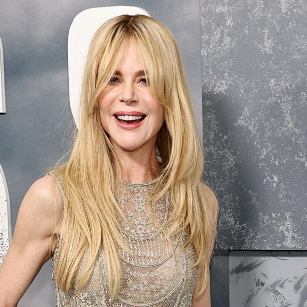 Nicole Kidman lächelt vor einem grauen Hintergrund mit großen weißen Buchstaben in die Kamera.