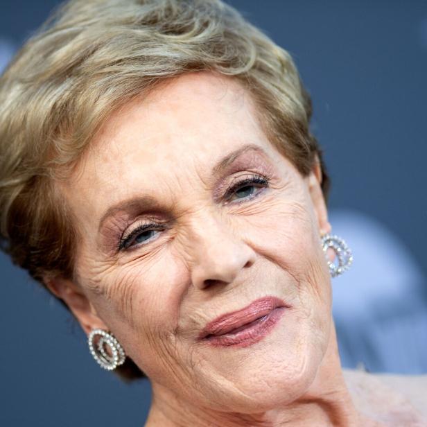 Nahaufnahme der Schauspielerin Julie Andrews mit kurzem blondem Haar und auffälligen Ohrringen vor einem dunklen Hintergrund.