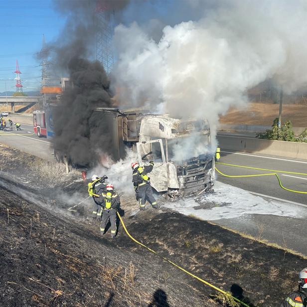 Feuerwehrleute löschen einen ausgebrannten Lkw auf der S1, während dichter Rauch von der Böschung aufsteigt.