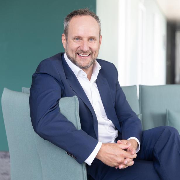 Lächelnder Mann im blauen Anzug sitzt auf einem hellgrünen Sofa in einem modernen Büro.
