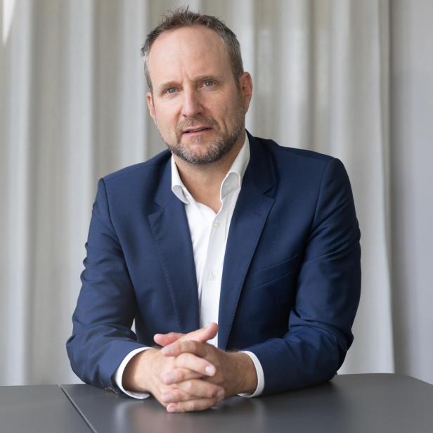 Mann im blauen Anzug sitzt am Tisch und blickt ernst in die Kamera.