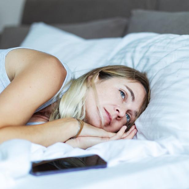 Mid adult woman lying in bed with mobile in depression