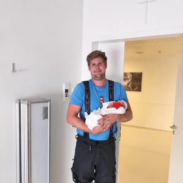 Feuerwehrmann in Einsatzkleidung hält sein neugeborenes Kind im Krankenhaus in den Armen.