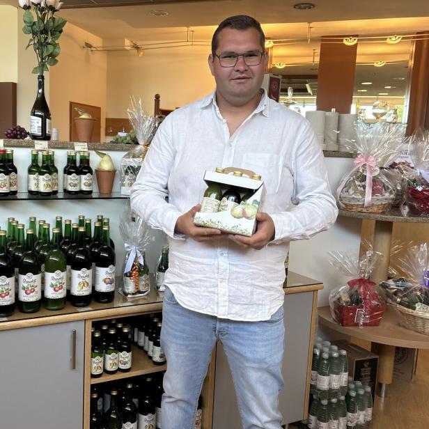 Saftproduzent Martin Trummer weißem Hemd hält eine Geschenkbox mit Flaschen in einem Laden für Getränke und Geschenkkörbe.