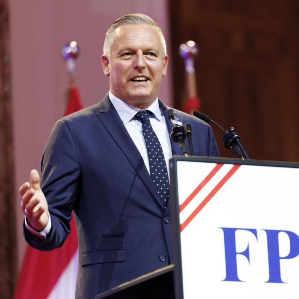 Mann im Anzug spricht an einem Rednerpult vor Mikrofonen und FPÖ-Logo.