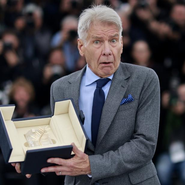 Harrison Ford hält mit überraschtem Gesichtsausdruck die Goldene Palme bei den Filmfestspielen von Cannes in die Kamera.