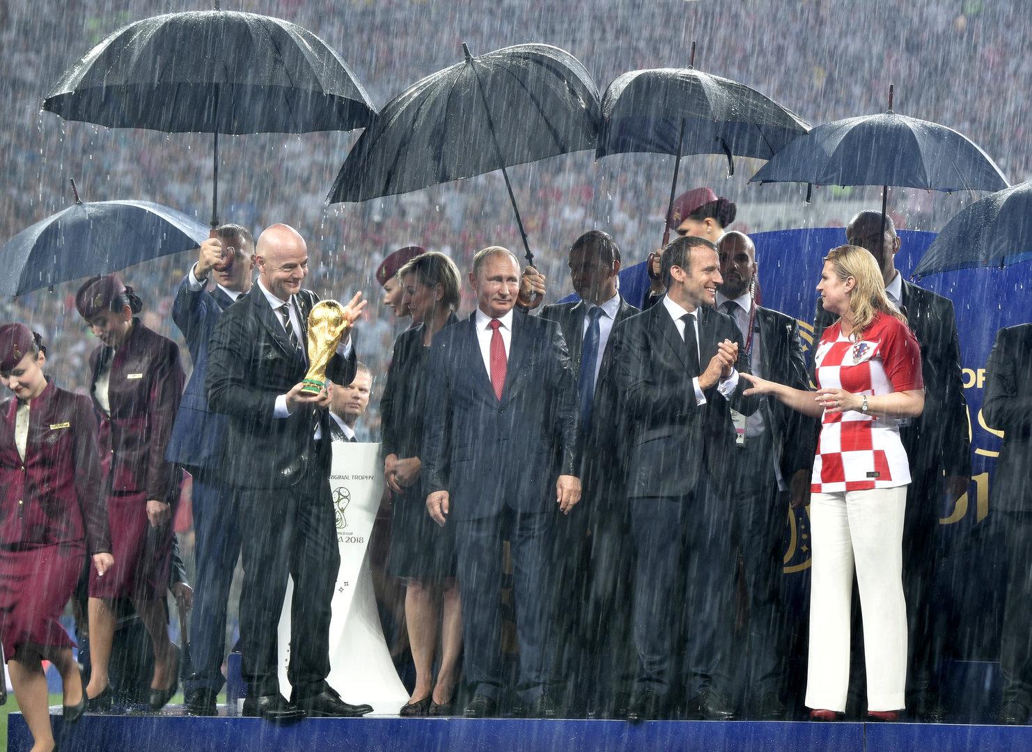 Wladimir Putin, Gianni Infantino und Emmanuel Macron stehen im Regen bei der Siegerehrung der Fußball-Weltmeisterschaft.