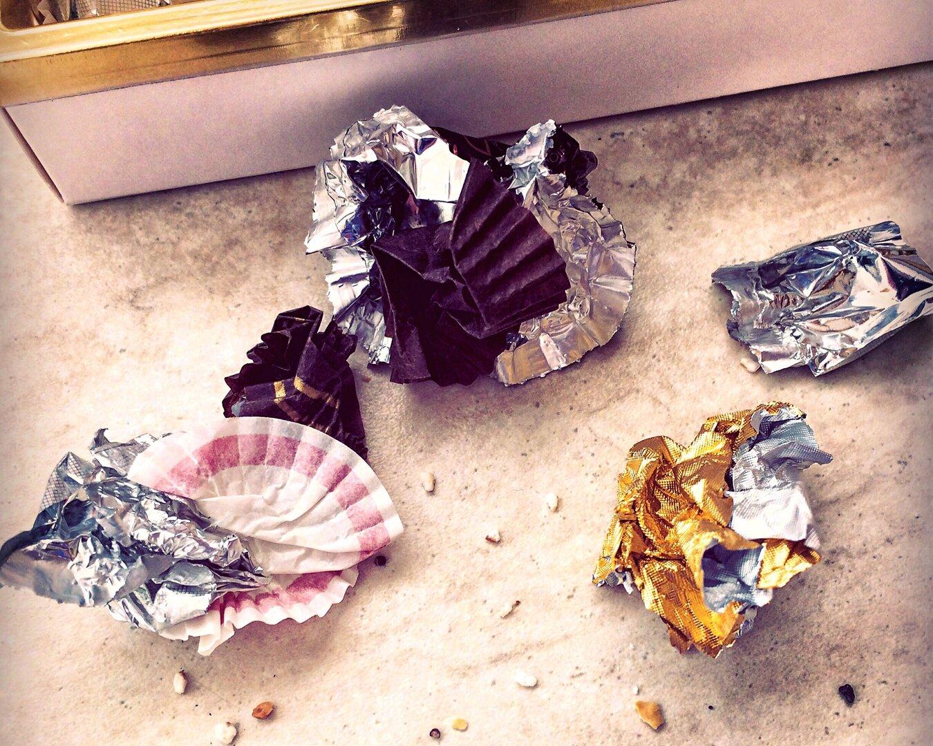 Leere Pralinenverpackungen und Krümel liegen auf einer Oberfläche.