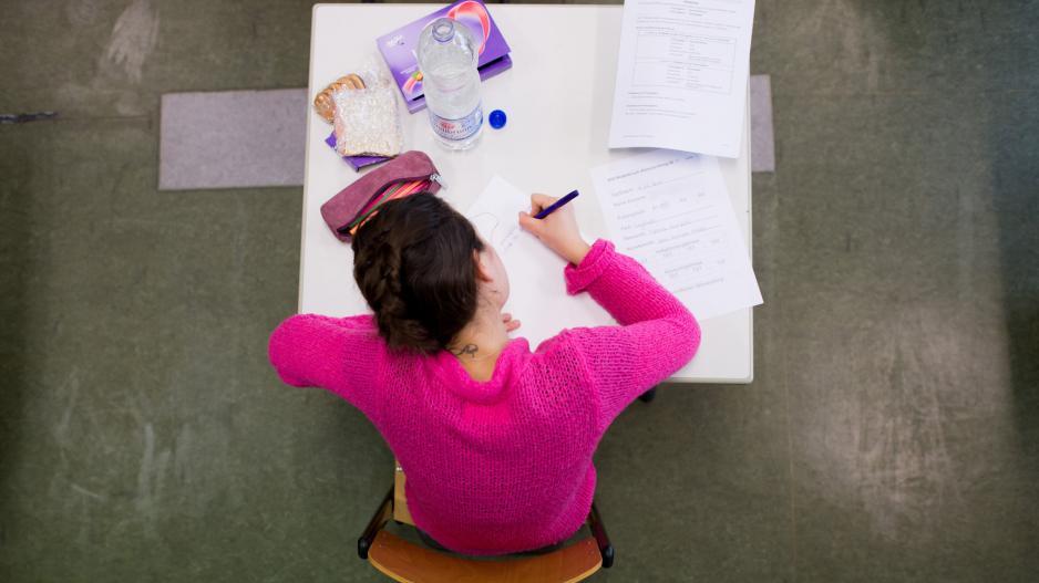 Eine Schülerin sitzt an einem Tisch und schreibt auf ein Blatt Papier.