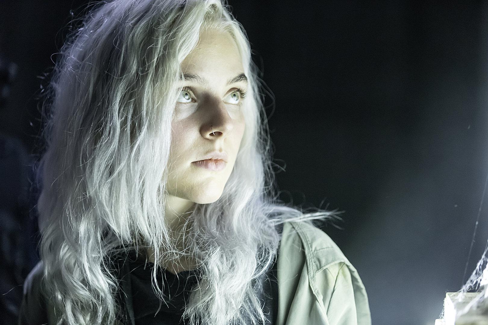 Eine Frau mit silberblondem Haar und Nasenpiercing blickt nach oben.