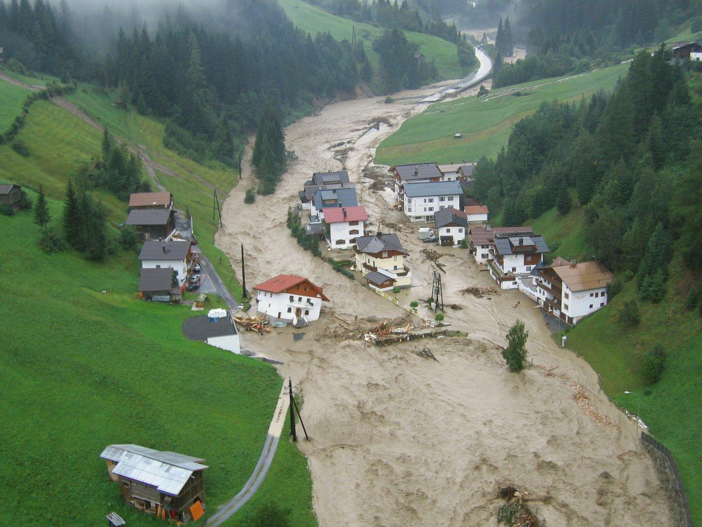 Hochwasser hat ein Dorf in einer grünen Hügellandschaft überflutet.