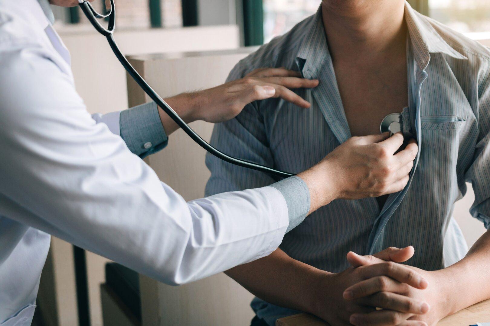 Arzt untersucht mit Stethoskop den Brustkorb eines sitzenden Patienten.