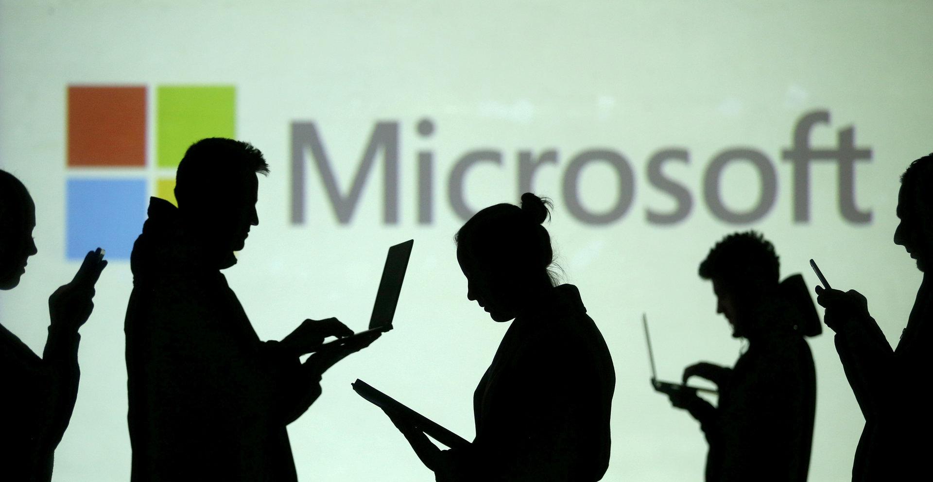 FILE PHOTO: FILE PHOTO: Silhouettes of laptop and mobile device users are seen next to a screen projection of Microsoft logo in this picture illustration