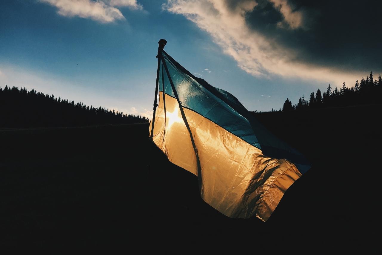 Die ukrainische Flagge weht vor einer Waldkulisse im Gegenlicht.
