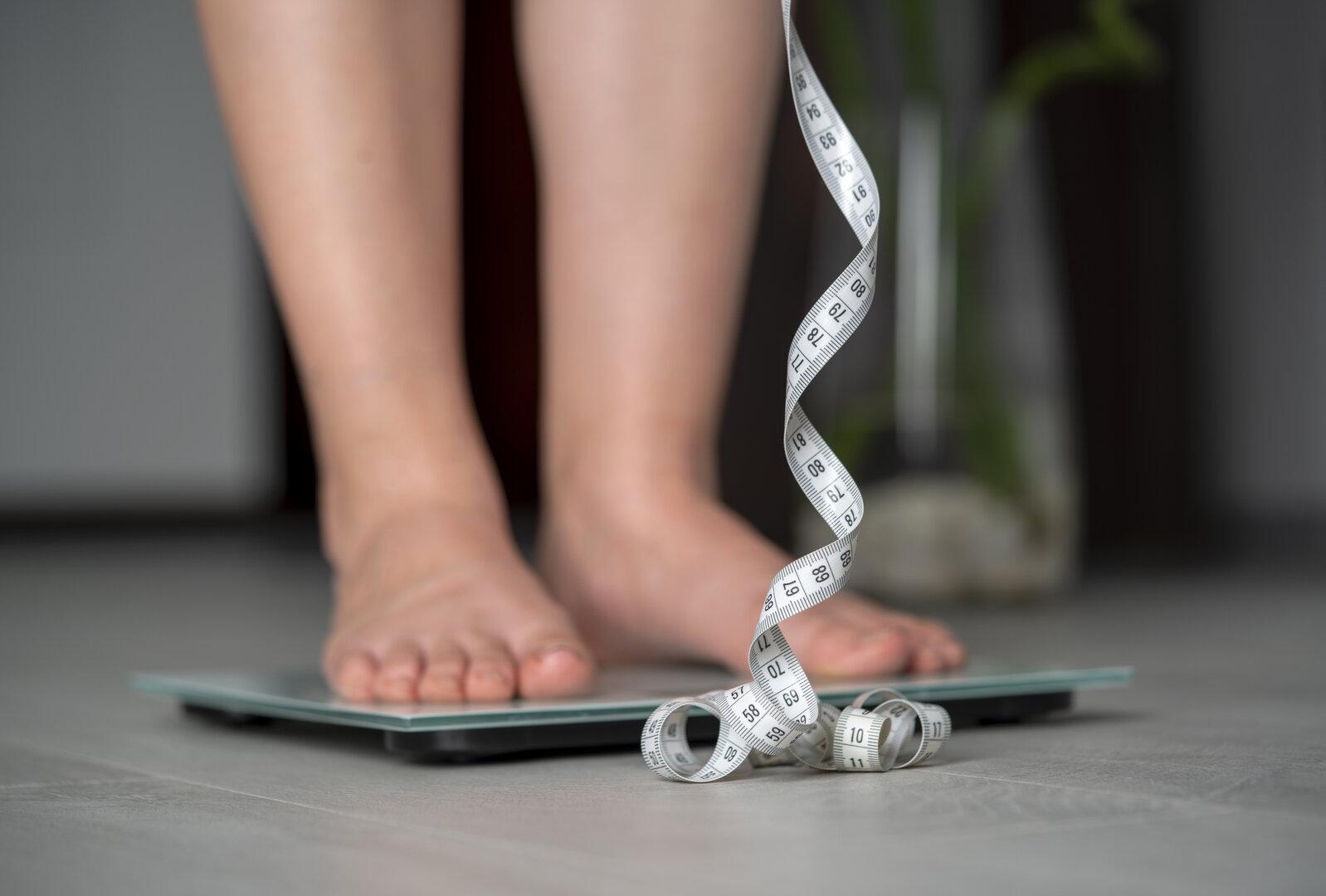 Weibliche Person steht auf Waage, man sieht nur die Füße und ein Maßband