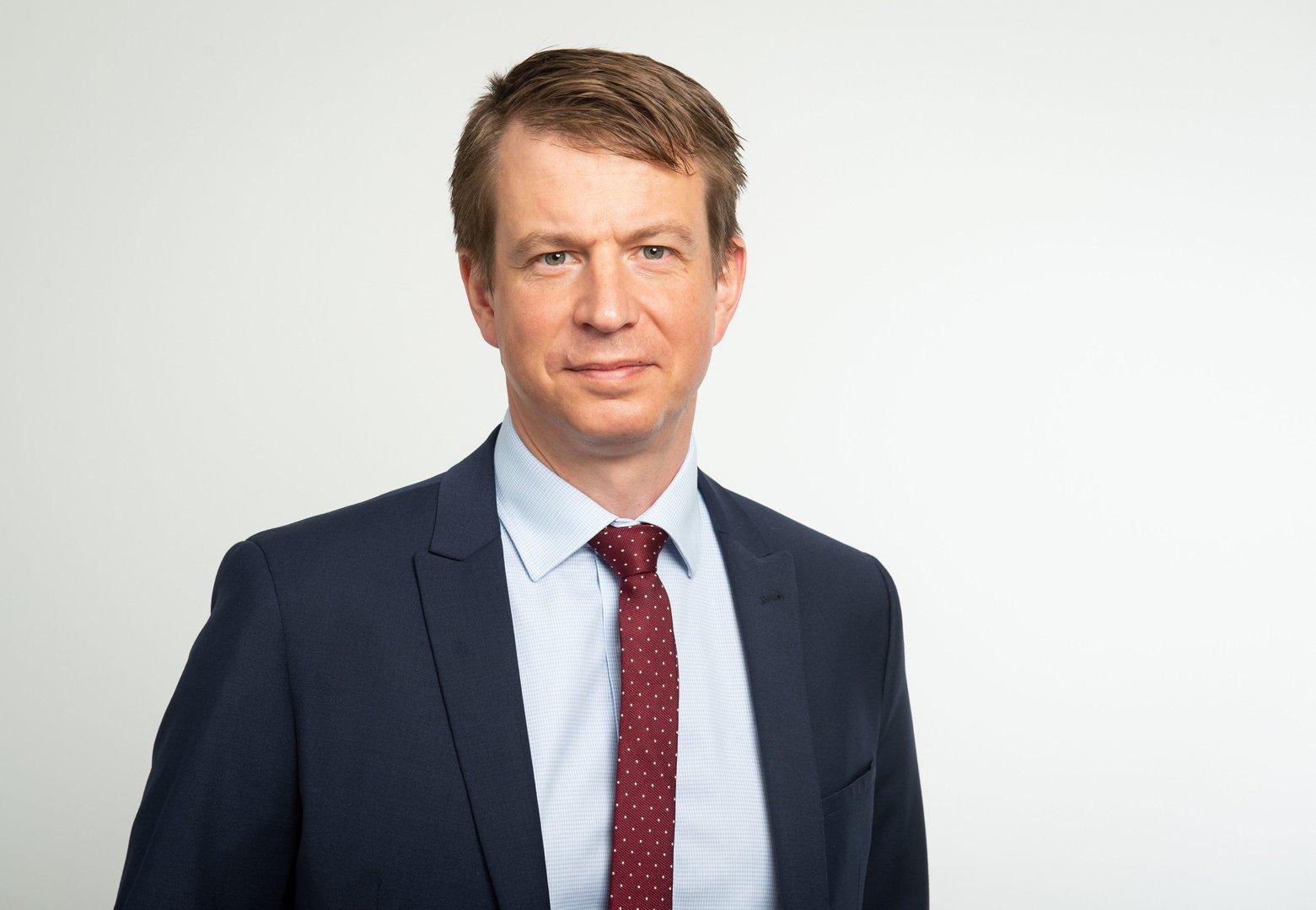 Ein Mann mit Anzug und Krawatte blickt in die Kamera.