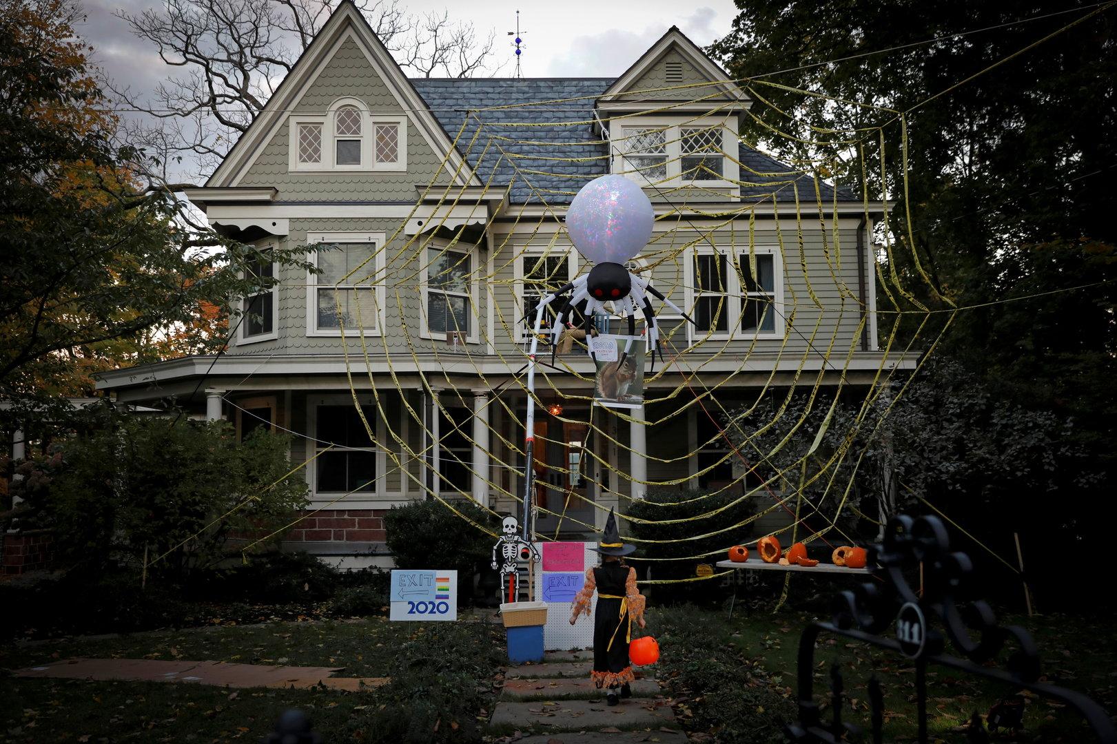 A trick-or-treater dressed as a witch approaches a home decorated with a giant spider web in Nyack