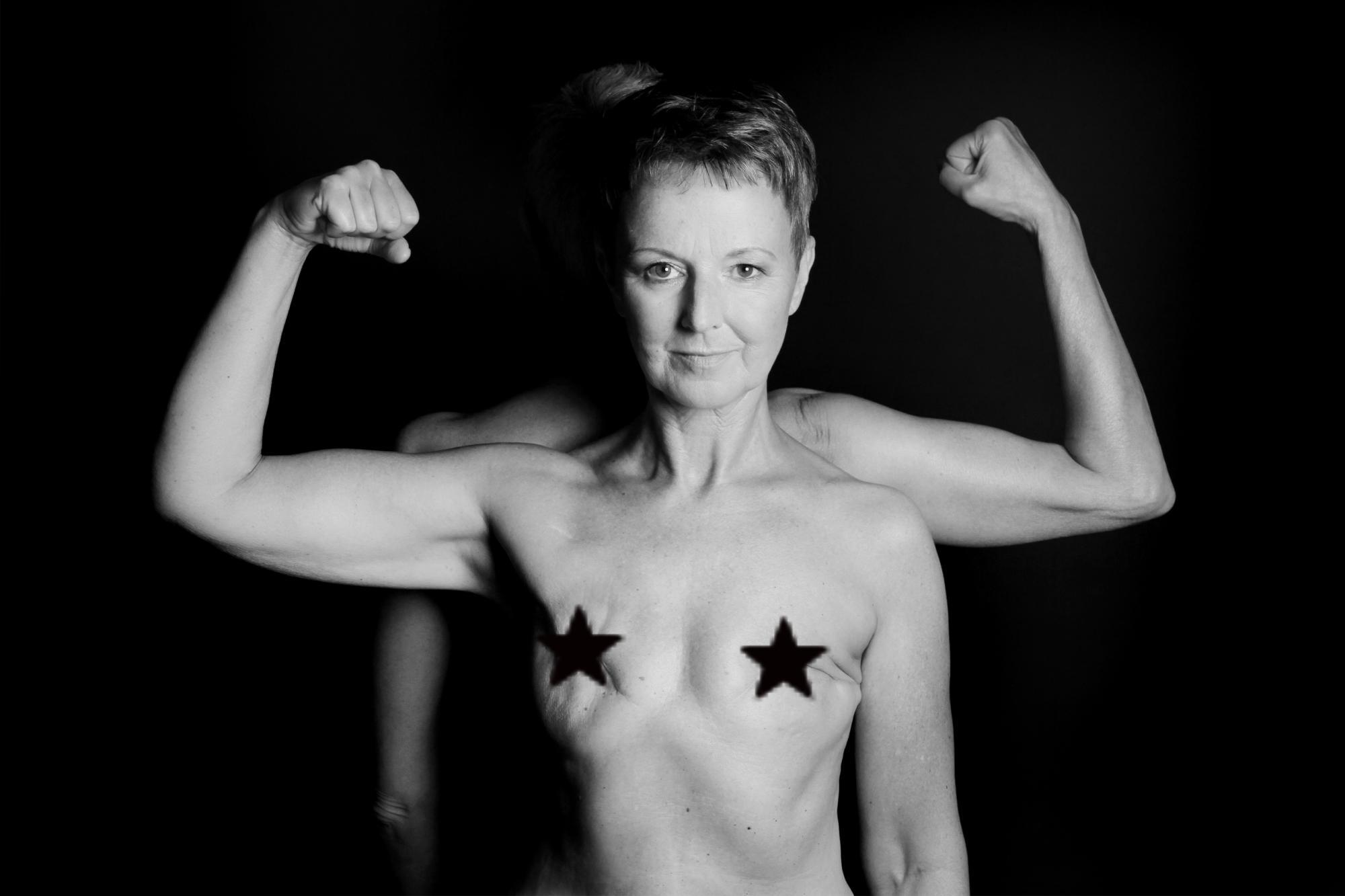 Eine Frau mittleren Alters präsentiert ihre Muskeln vor einem dunklen Hintergrund.