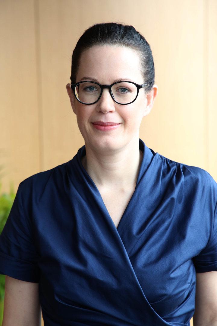 Eine Frau mit Brille und blauem Oberteil lächelt in die Kamera.