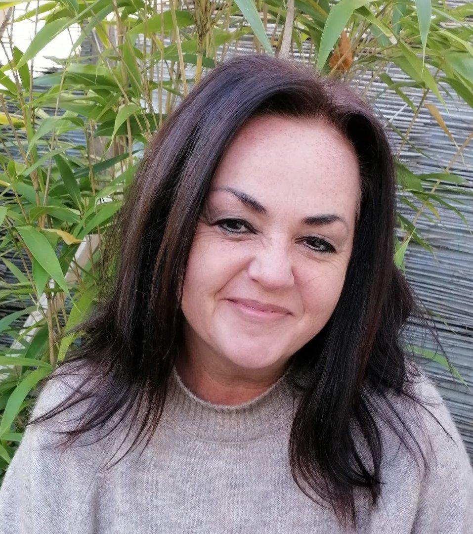 Eine lächelnde Frau mit dunklen Haaren vor einem Bambushintergrund.