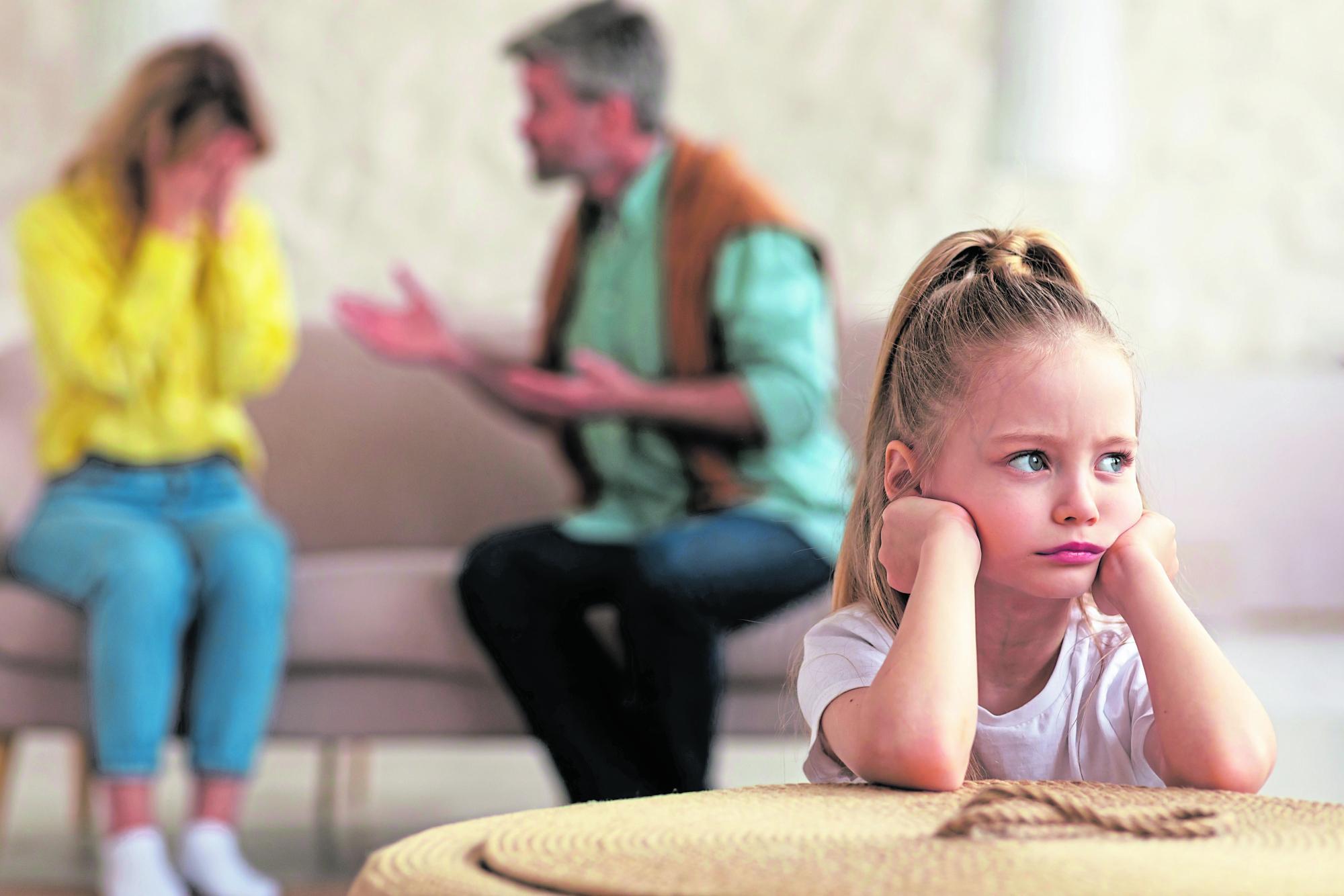 Streitende Eltern im Hintergrund, während ihre unglückliche Tochter traurig am Tisch sitzt.