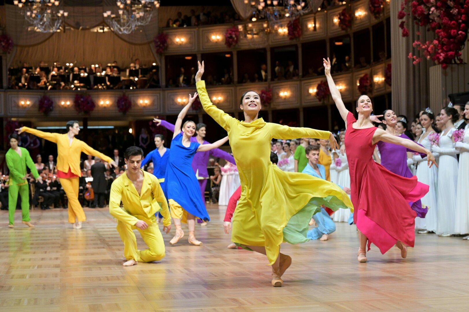 Eine Gruppe Tänzerinnen und Tänzer in farbenfrohen Kostümen auf einer Bühne.