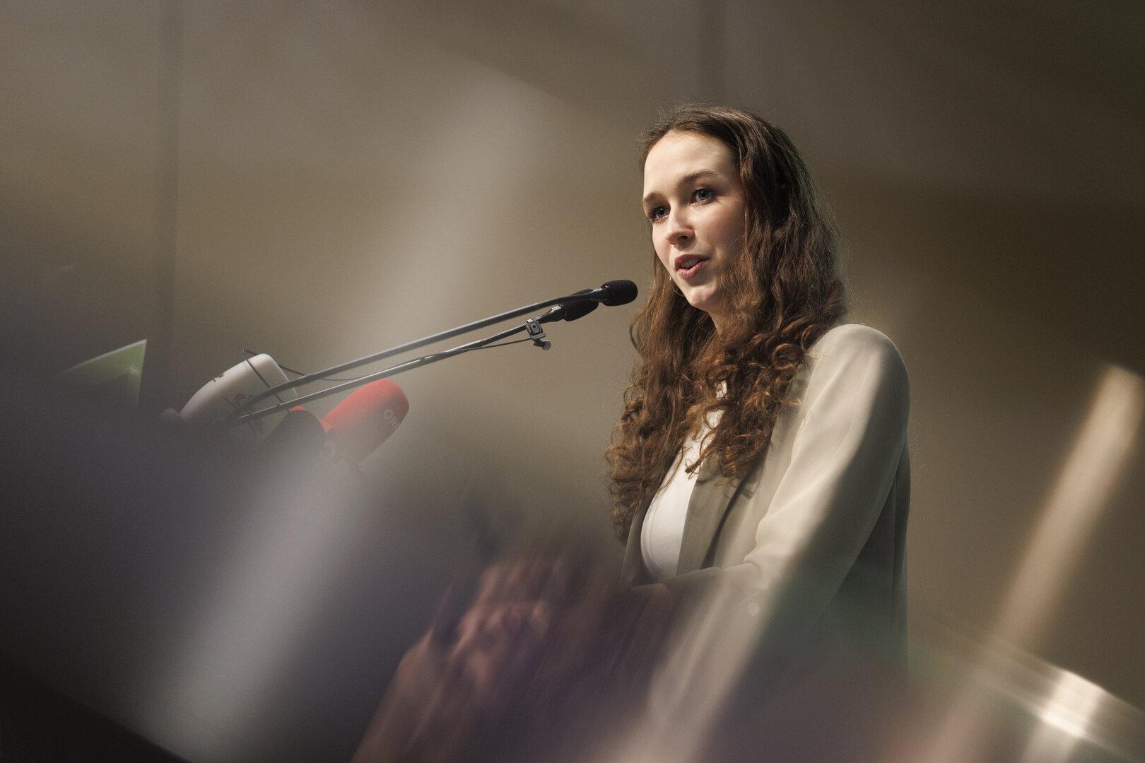 Eine junge Frau spricht bei einer Pressekonferenz in ein Mikrofon.