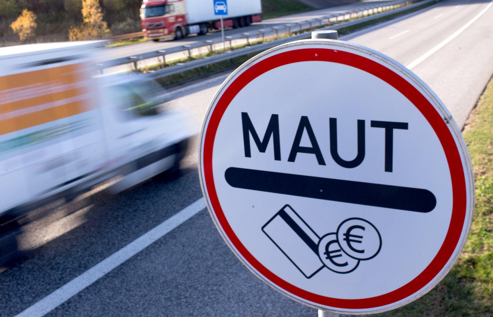 Ein rundes Verkehrsschild mit der Aufschrift „MAUT“ und Symbolen für Bezahlung steht an einer Autobahn.