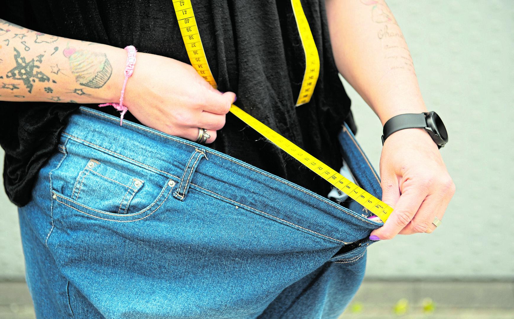 Eine Frau misst mit einem Maßband den Abstand einer viel zu großen Hose von ihrem Bauch.