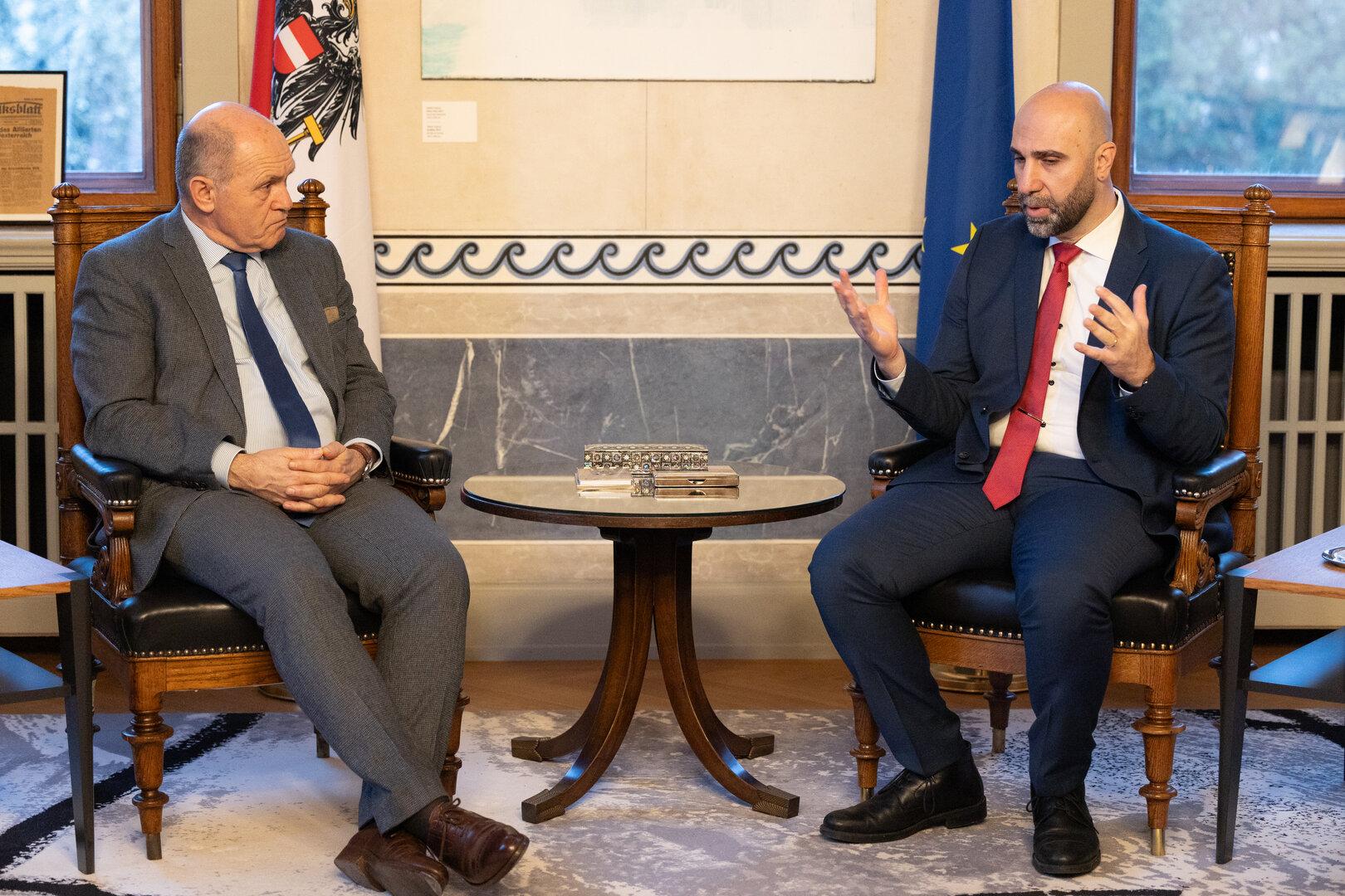 Zwei Männer sitzen sich gegenüber und diskutieren in einem formellen Rahmen.