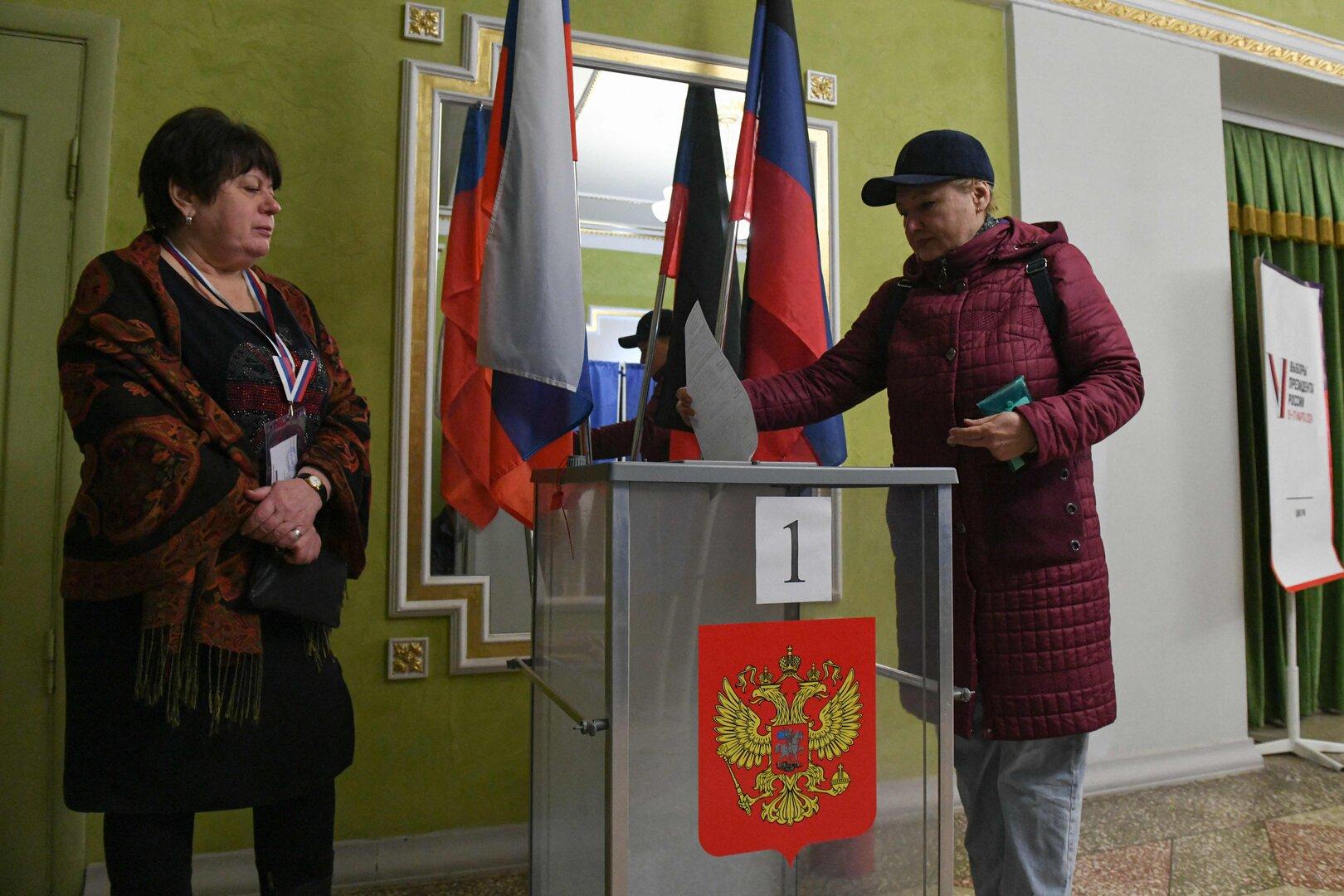 Eine Frau wirft ihren Stimmzettel in eine Wahlurne mit dem russischen Wappen.