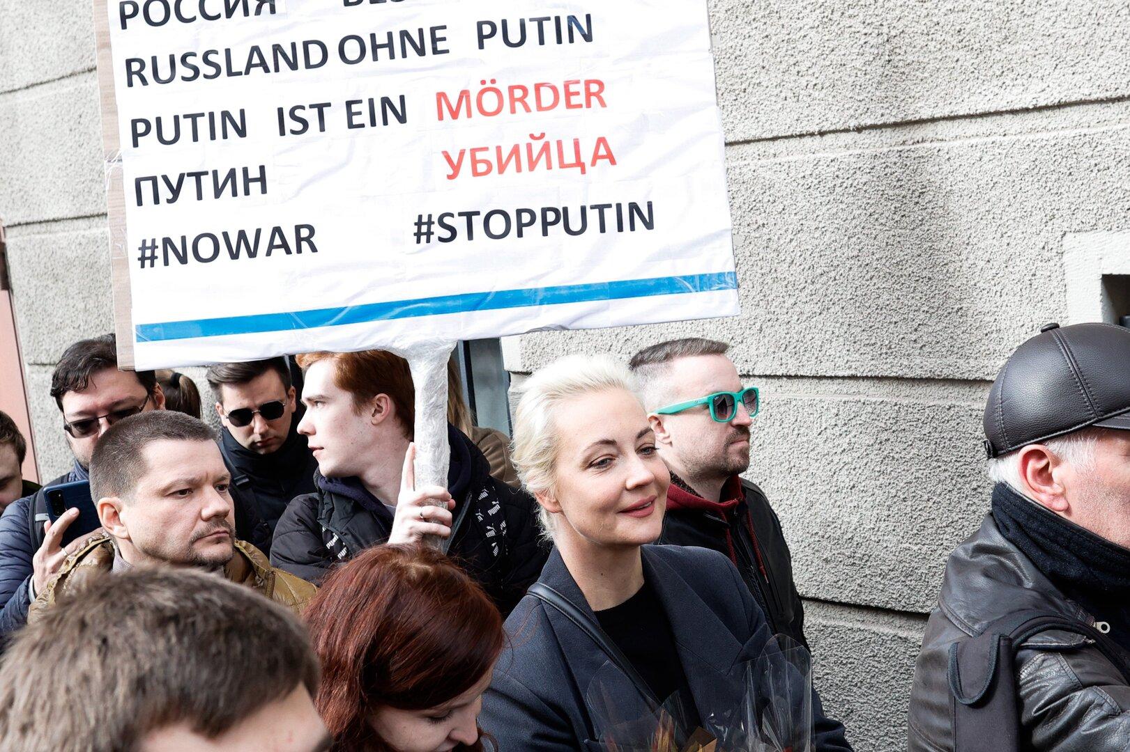 Menschen demonstrieren mit einem Schild, auf dem „Russland ohne Putin“ und „Putin ist ein Mörder“ steht.