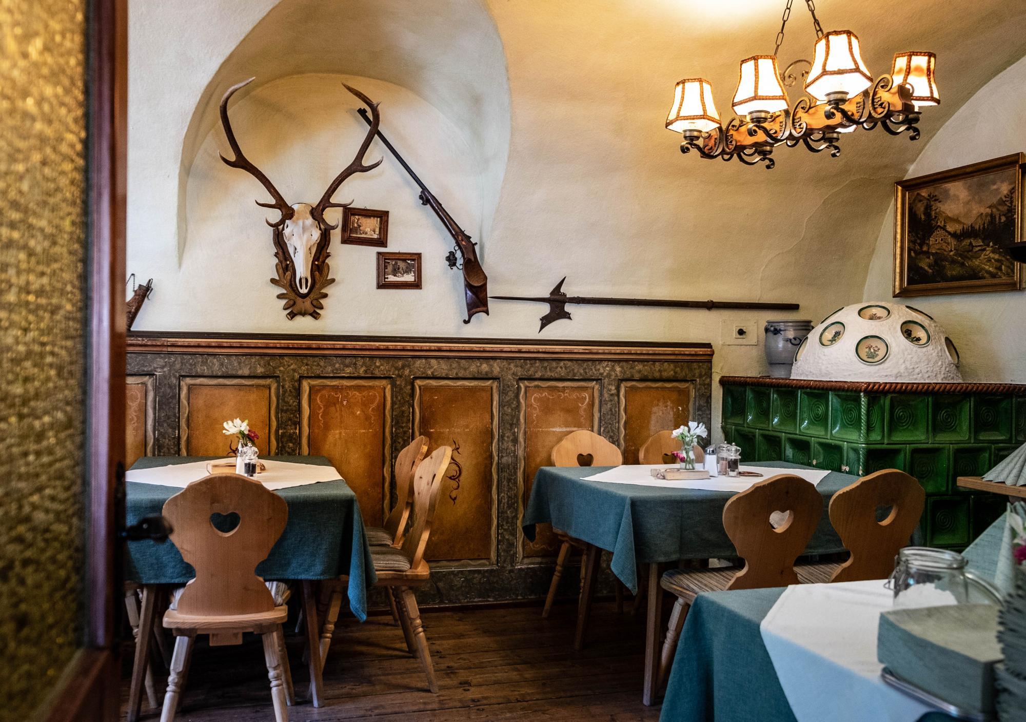 Innenansicht eines traditionellen Wirtshauses mit Geweih, Waffen und Kachelofen.