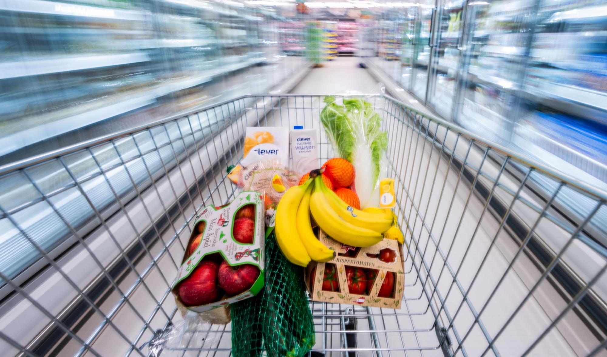 Ein Einkaufswagen voller Lebensmittel wird durch einen Supermarkt geschoben.