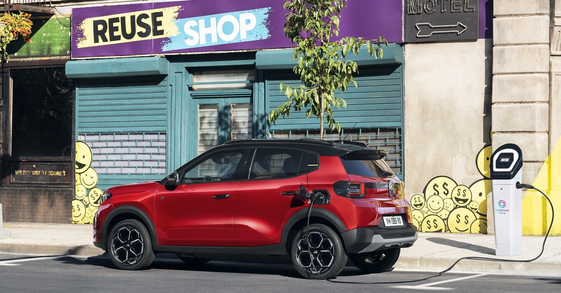 Ein roter Jeep Avenger wird an einer Ladestation vor einem „Reuse Shop“ aufgeladen.