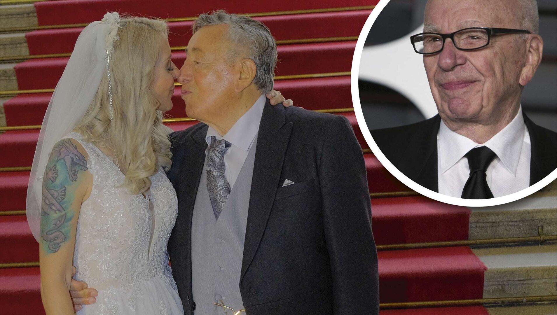 Ein Hochzeitspaar steht vor einer Treppe mit rotem Teppich, im Hintergrund ein Porträt von Rupert Murdoch.