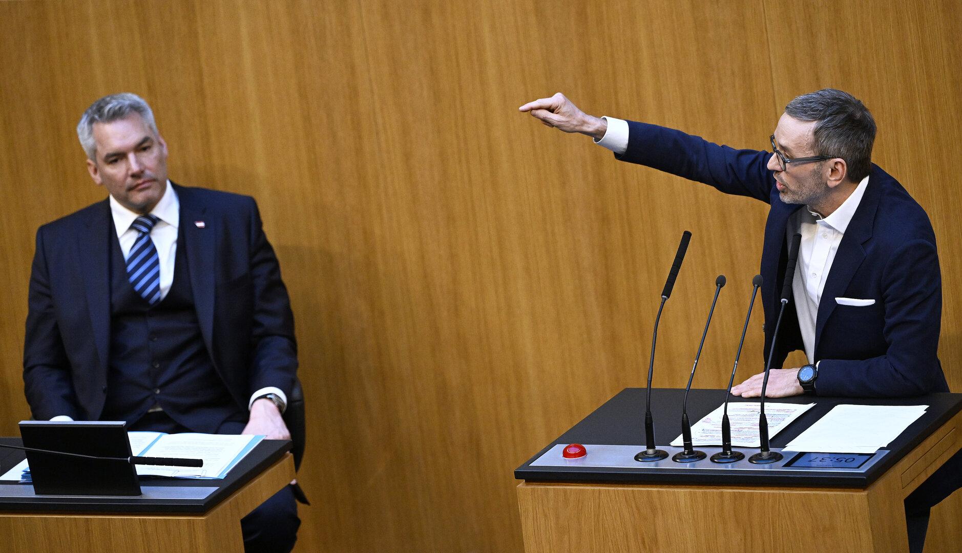 Zwei Männer in Anzügen sitzen in einem holzvertäfelten Raum, einer gestikuliert.