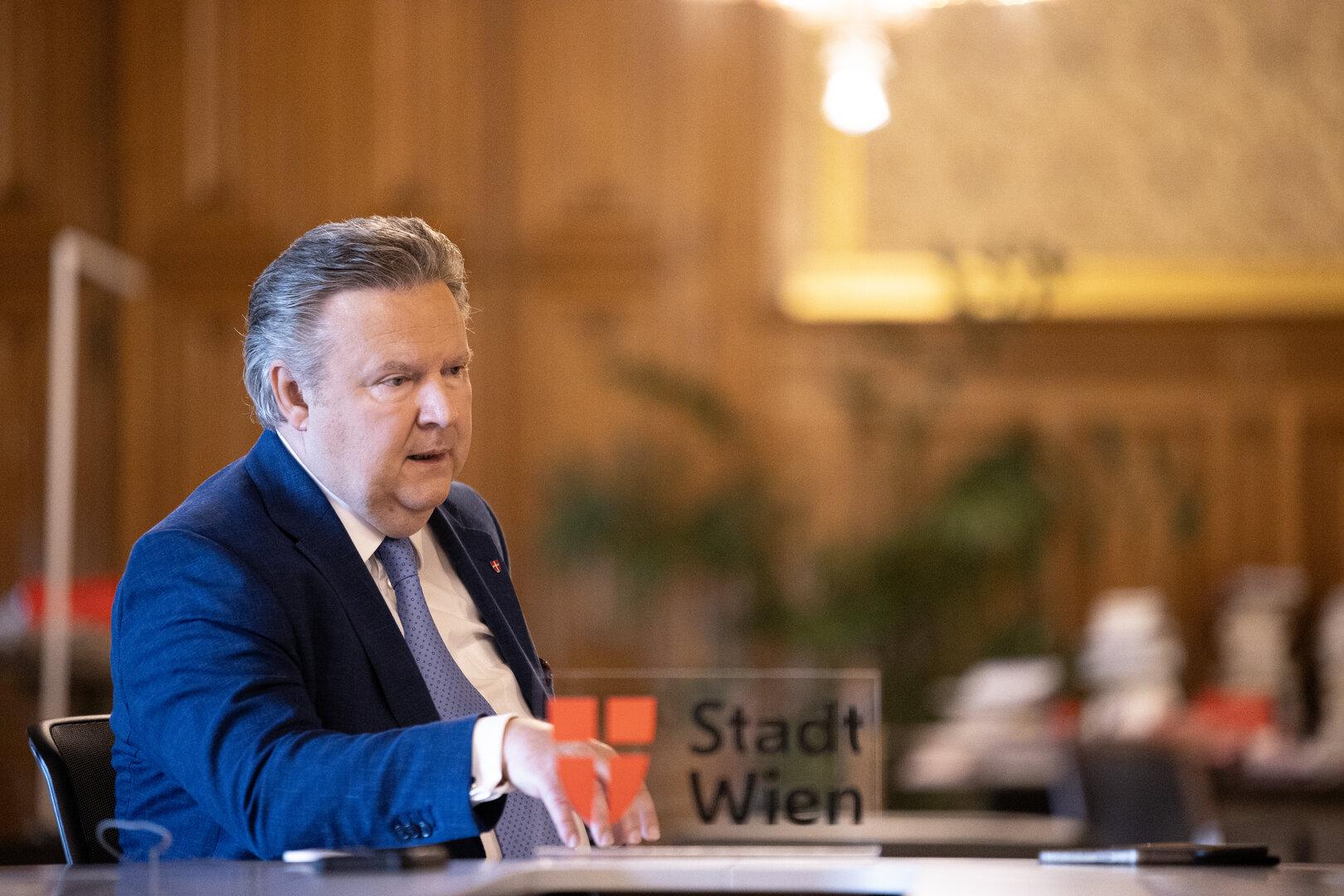 Ein Mann im Anzug sitzt an einem Tisch mit dem Logo der Stadt Wien.