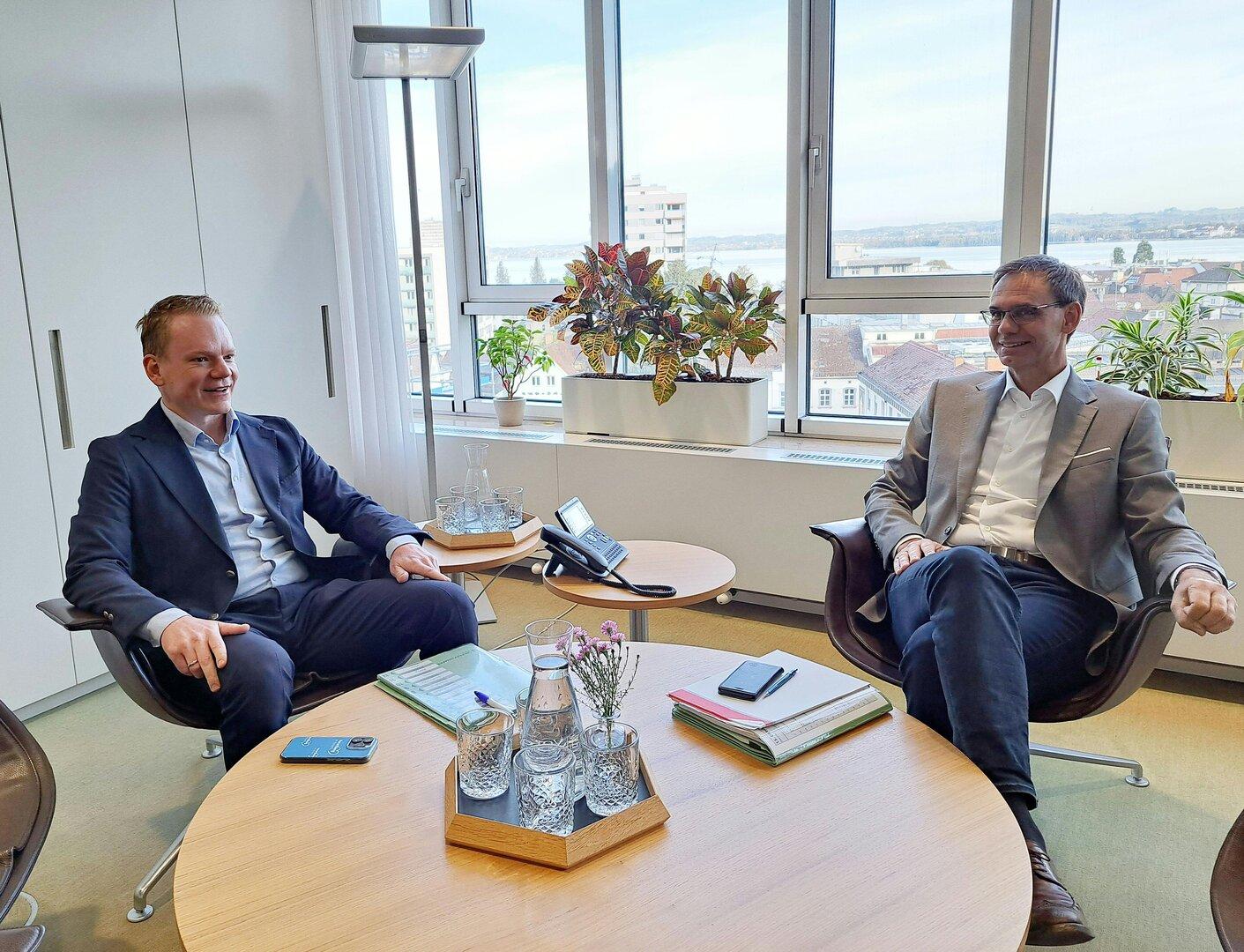 Zwei Männer sitzen an einem Tisch in einem Büro und unterhalten sich.