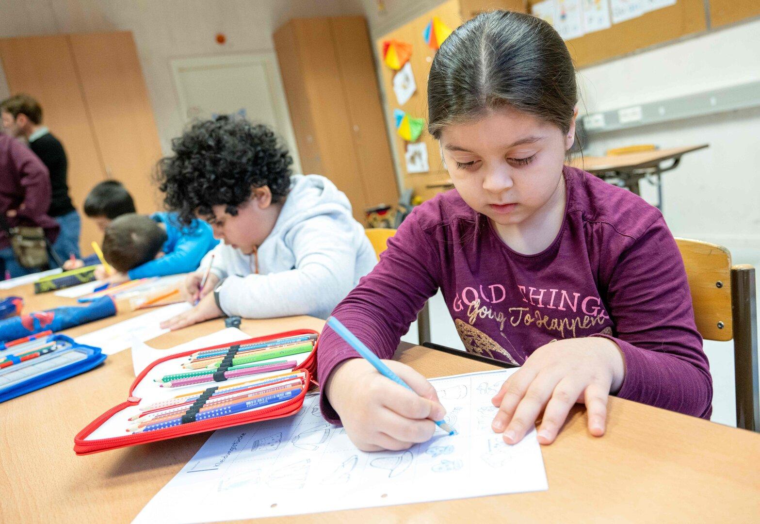 Ein Mädchen sitzt im Klassenzimmer und malt mit Buntstiften.