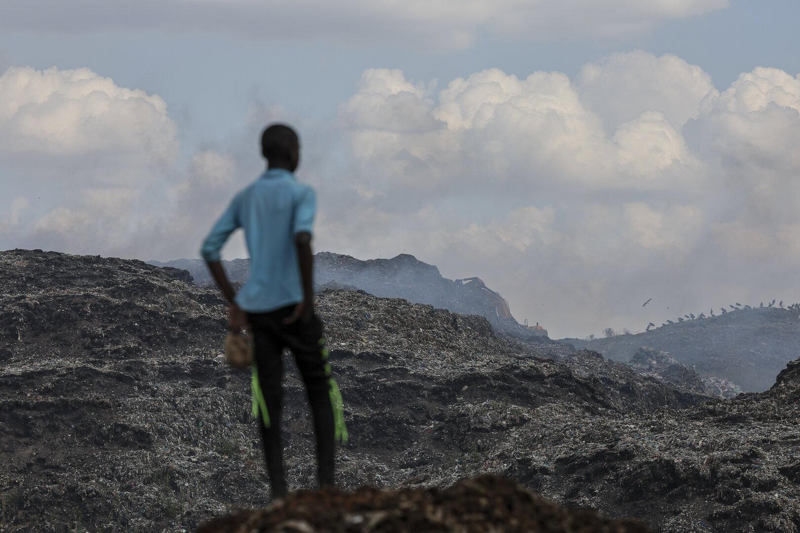 Ein Junge steht auf einer Müllhalde und blickt in die Ferne.