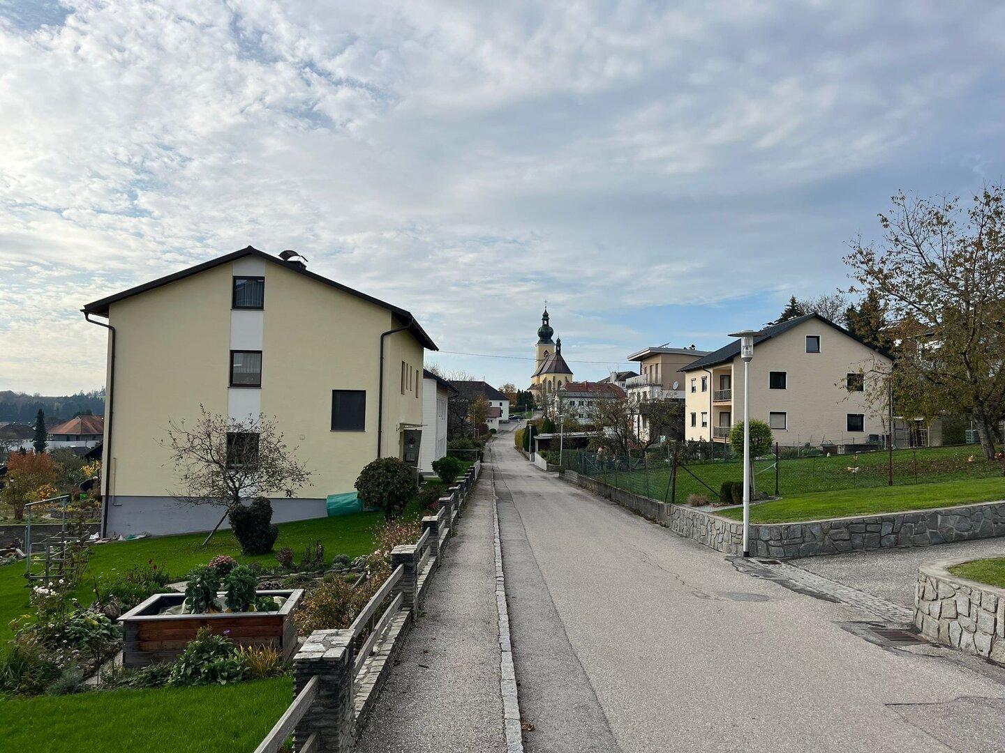 Eine Straße führt durch eine ruhige Wohngegend mit einer Kirche im Hintergrund.