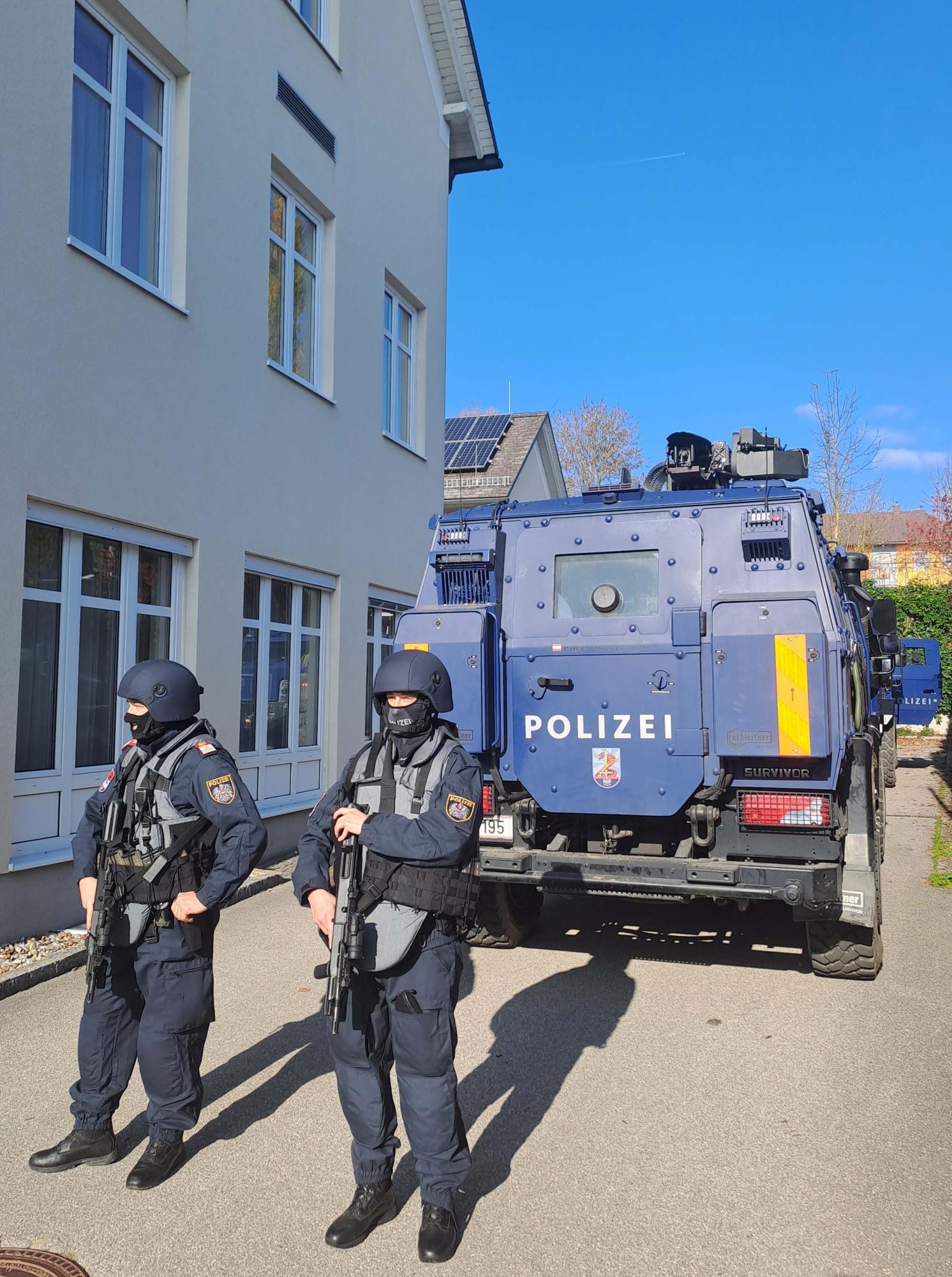 Zwei Polizisten stehen vor einem gepanzerten Polizeifahrzeug.
