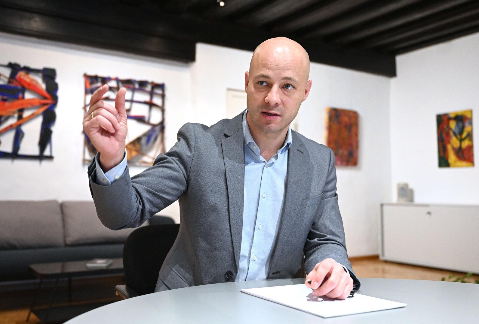 Ein Mann im Anzug gestikuliert an einem Tisch in einem Büro.